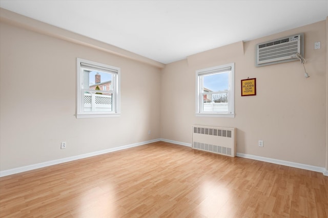 spare room with baseboards, light wood-style flooring, radiator heating unit, and a wall mounted AC