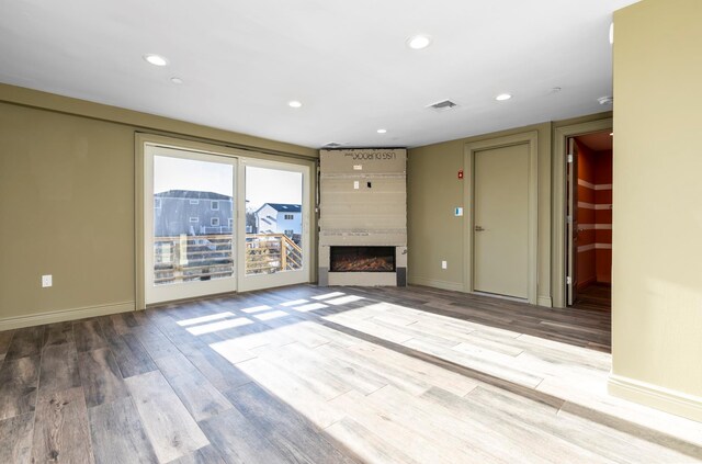 unfurnished living room with recessed lighting, a large fireplace, baseboards, and wood finished floors