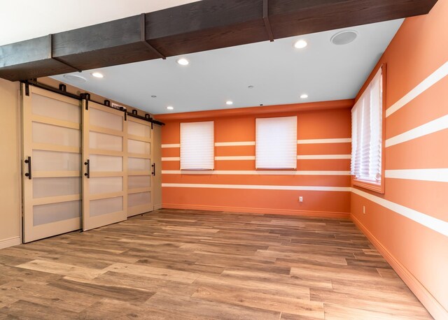 spare room featuring recessed lighting, a barn door, baseboards, and wood finished floors