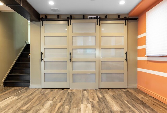 below grade area featuring recessed lighting, stairway, a barn door, wood finished floors, and baseboards