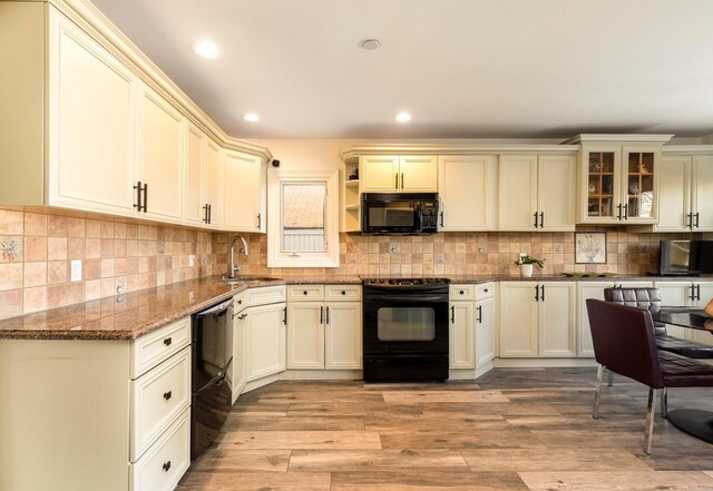 kitchen with a sink, light wood-type flooring, black appliances, and dark stone counters
