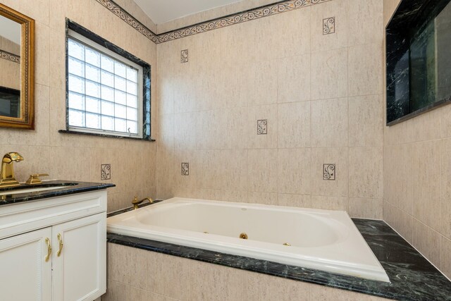 bathroom with a whirlpool tub, vanity, and tile walls