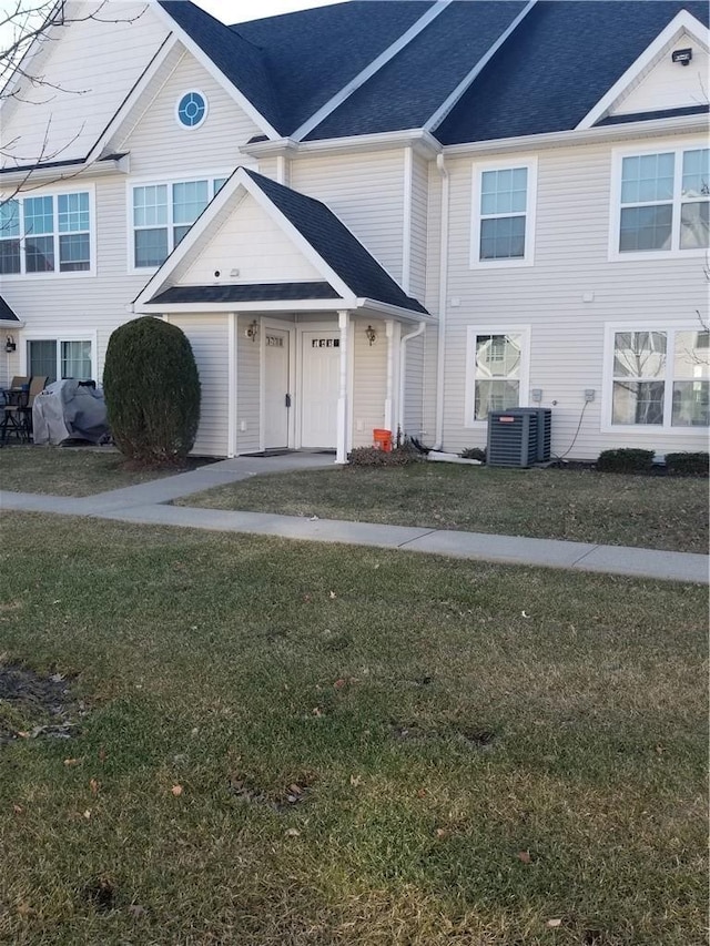 multi unit property with cooling unit, roof with shingles, an attached garage, and a front lawn