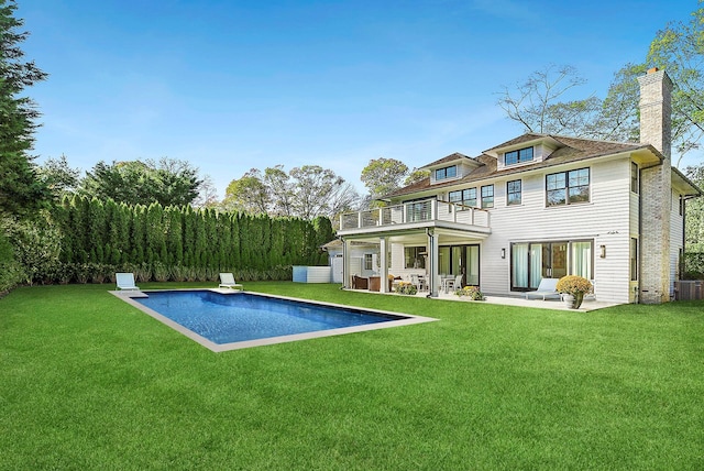 rear view of house featuring a lawn, a balcony, and an outdoor pool