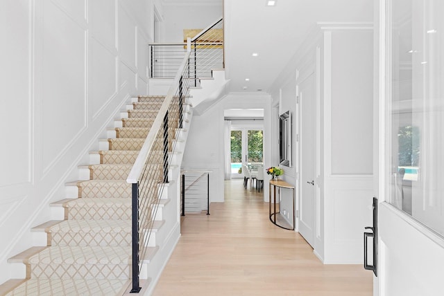 foyer entrance featuring crown molding, light wood finished floors, recessed lighting, a decorative wall, and stairway