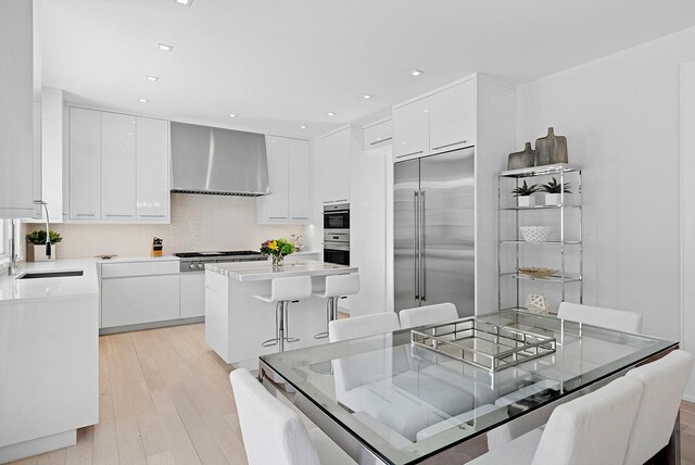 kitchen with wall chimney range hood, modern cabinets, stainless steel appliances, and a kitchen breakfast bar