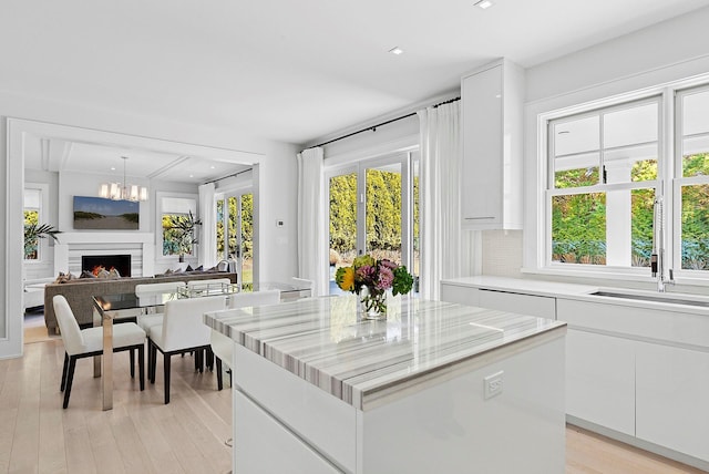 kitchen with light wood-style flooring, a sink, white cabinetry, a lit fireplace, and a center island