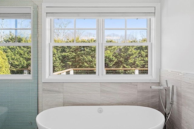 bathroom with a wealth of natural light, a soaking tub, and tile walls