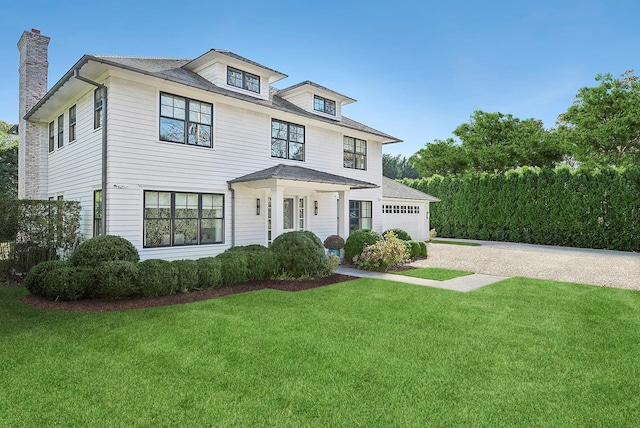 traditional style home with a garage, driveway, a chimney, and a front lawn