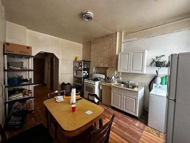 kitchen with white gas stove, a sink, light wood-style floors, freestanding refrigerator, and washer / clothes dryer