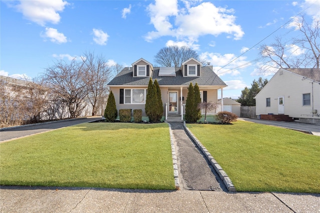 new england style home featuring driveway, solar panels, a front lawn, and a shingled roof