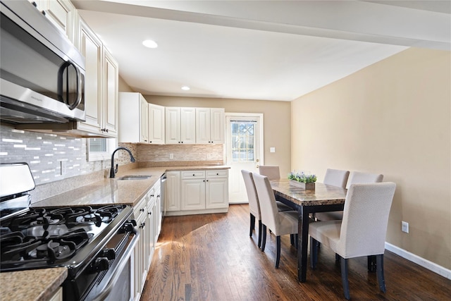 kitchen with dark wood-type flooring, a sink, tasteful backsplash, appliances with stainless steel finishes, and white cabinets