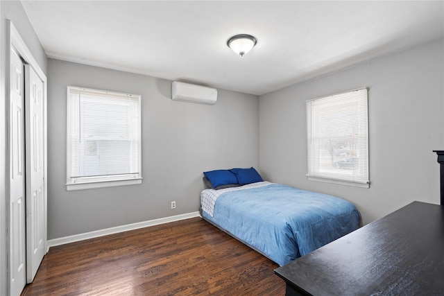 bedroom with an AC wall unit, wood finished floors, baseboards, and a closet