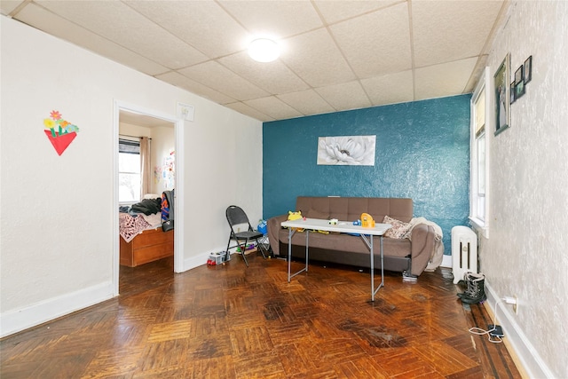 bedroom featuring radiator, an accent wall, baseboards, and a drop ceiling