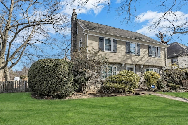 colonial inspired home featuring a front yard, fence, and a chimney