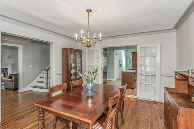 dining space with baseboards, stairs, ornamental molding, wood finished floors, and a notable chandelier