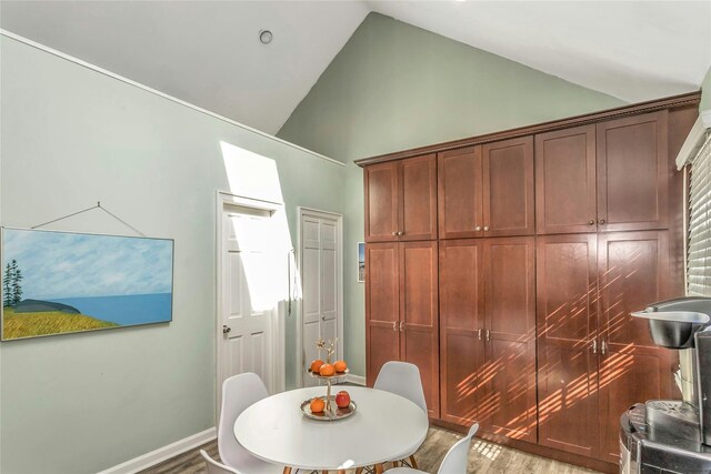 dining space with baseboards, high vaulted ceiling, and wood finished floors