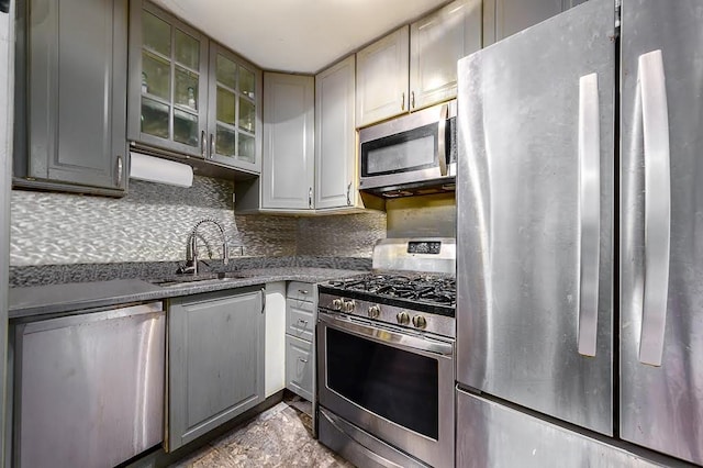 kitchen with stainless steel appliances, gray cabinets, a sink, and decorative backsplash