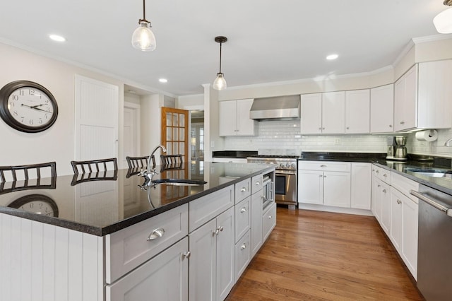 kitchen featuring crown molding, wall chimney range hood, light wood-style flooring, stainless steel appliances, and a sink