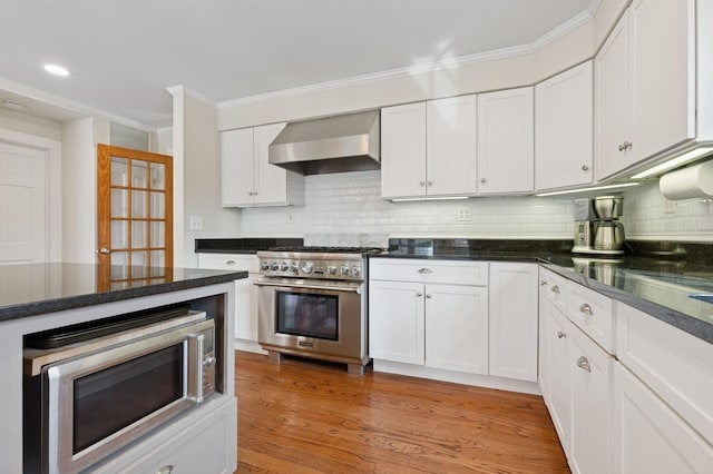 kitchen featuring crown molding, wall chimney range hood, white cabinets, and appliances with stainless steel finishes