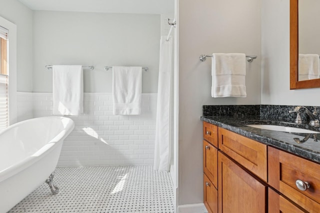 full bathroom with tile patterned floors, a freestanding tub, a wainscoted wall, tile walls, and vanity