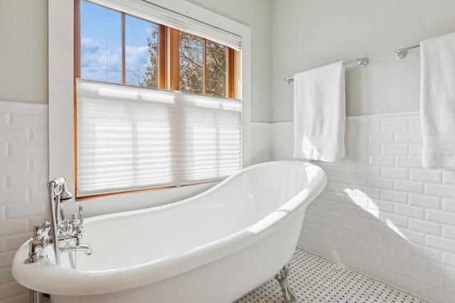 full bath featuring tile patterned flooring, a soaking tub, wainscoting, and tile walls