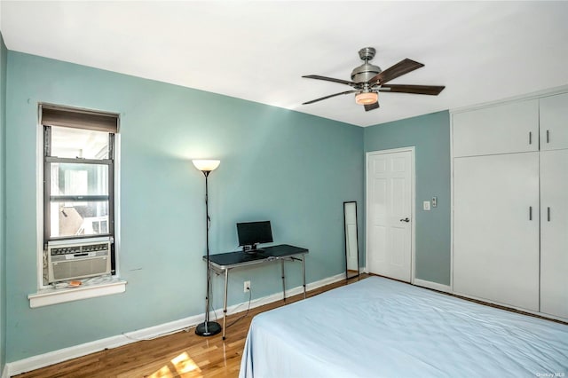 bedroom with cooling unit, wood finished floors, a ceiling fan, baseboards, and a closet