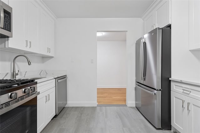 kitchen with white cabinets, light wood finished floors, stainless steel appliances, and a sink