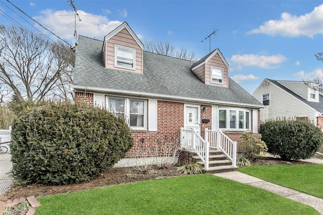 new england style home with a front yard, brick siding, and roof with shingles