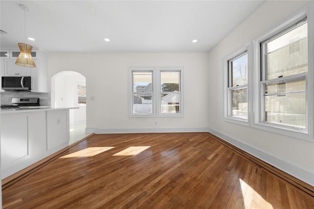 unfurnished living room with light wood-style floors, baseboards, arched walkways, and a wealth of natural light