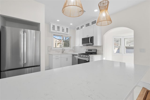 kitchen with pendant lighting, stainless steel appliances, decorative backsplash, glass insert cabinets, and a sink