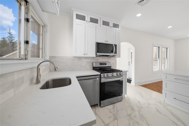 kitchen with arched walkways, a sink, visible vents, appliances with stainless steel finishes, and tasteful backsplash