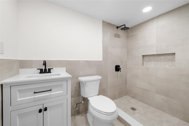 bathroom with tiled shower, vanity, toilet, and tile walls