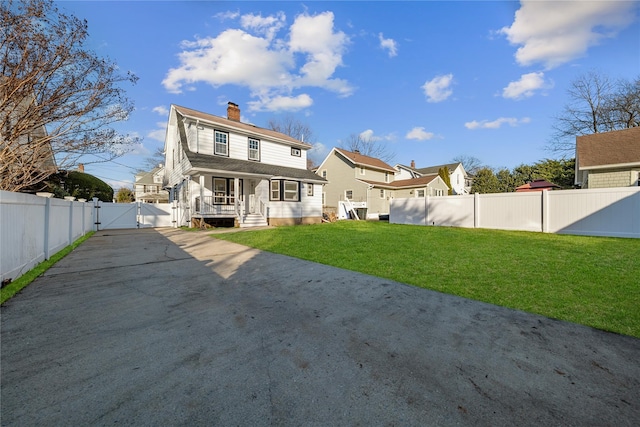 back of house with a gate, a chimney, fence, and a lawn