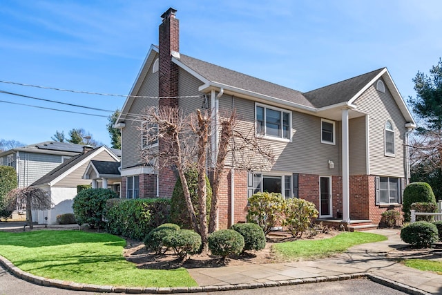 view of front of home featuring brick siding, a chimney, and a front yard