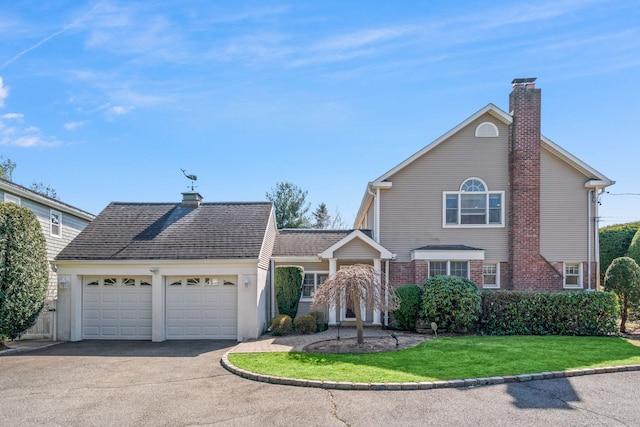 traditional-style home featuring a garage, brick siding, a chimney, and aphalt driveway