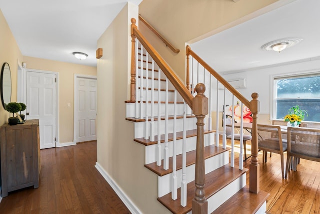 stairway with baseboards, hardwood / wood-style floors, and a wall unit AC