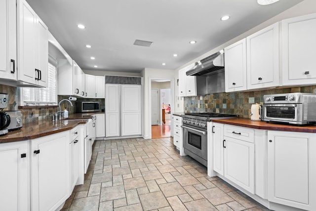 kitchen with wood counters, appliances with stainless steel finishes, wall chimney exhaust hood, and white cabinetry