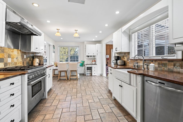 kitchen featuring butcher block countertops, a sink, white cabinetry, ventilation hood, and appliances with stainless steel finishes