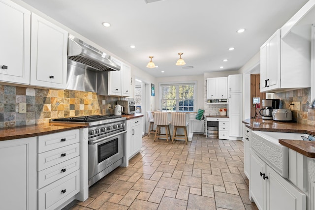 kitchen featuring tasteful backsplash, high end stove, exhaust hood, white cabinetry, and wood counters