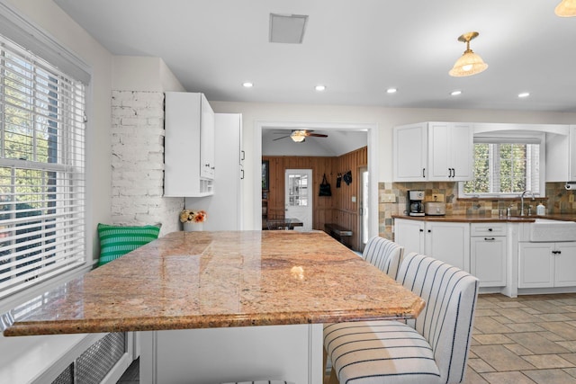 kitchen with white cabinetry, stone tile flooring, a breakfast bar area, and a sink