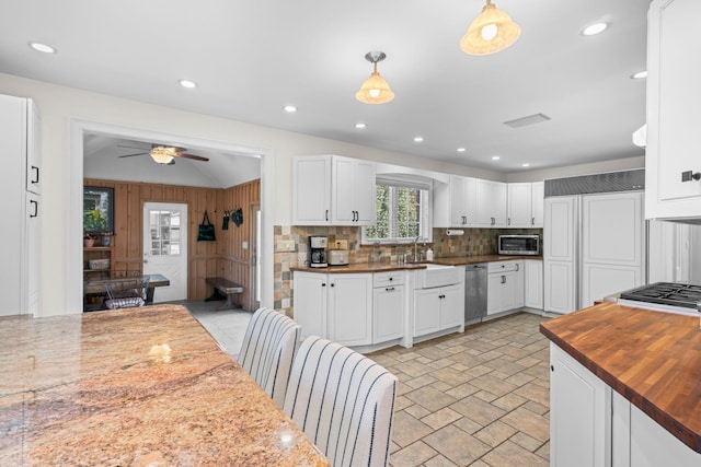 kitchen with butcher block countertops, a sink, stainless steel microwave, white cabinets, and decorative backsplash