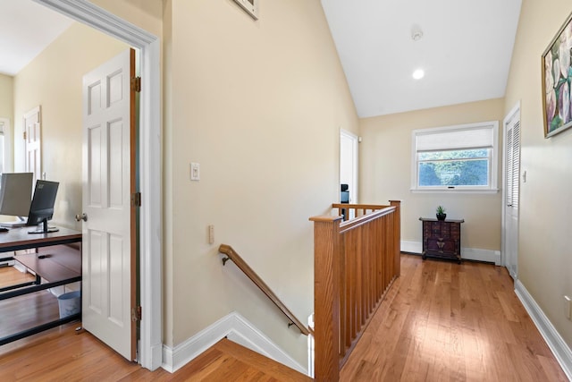 corridor with baseboards, an upstairs landing, vaulted ceiling, and light wood finished floors