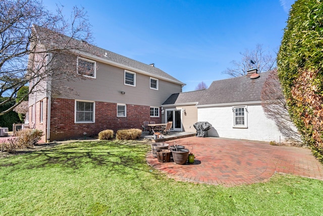 rear view of house with a patio area, a lawn, brick siding, and a chimney