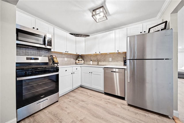 kitchen with appliances with stainless steel finishes, a sink, light countertops, white cabinetry, and backsplash