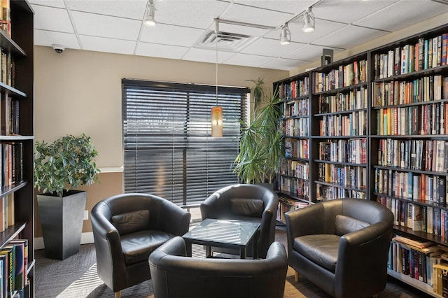 sitting room featuring bookshelves, visible vents, and a drop ceiling