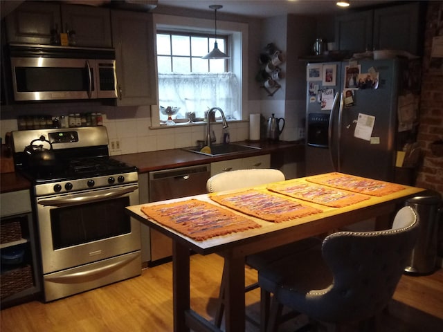 kitchen with dark countertops, backsplash, appliances with stainless steel finishes, a sink, and light wood-type flooring