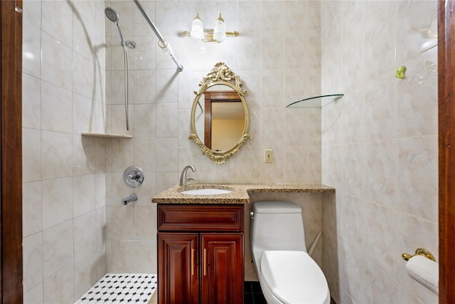 full bathroom with toilet, tiled shower, vanity, and tile walls