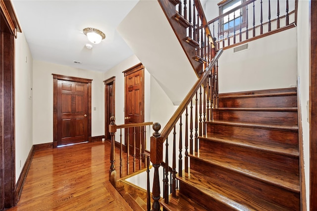 foyer featuring baseboards, stairs, visible vents, and wood finished floors