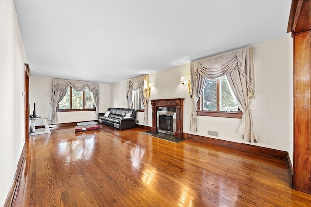 living area featuring a baseboard radiator, wood finished floors, a fireplace with flush hearth, visible vents, and baseboards